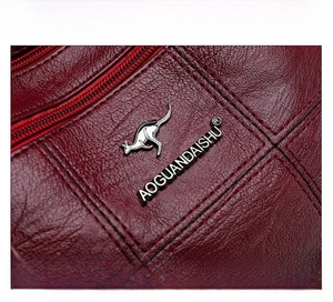 Detail of burgundy leather texture with silver kangaroo logo and fine stitching