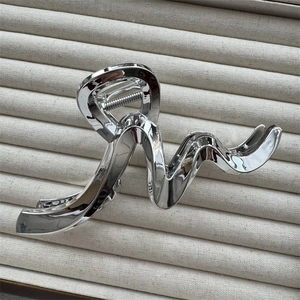 Close-up of a wavy silver metallic hair claw clip on a beige textured display surface