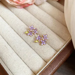 Elegant purple enamel flower stud earrings with green leaves on a jewelry stand