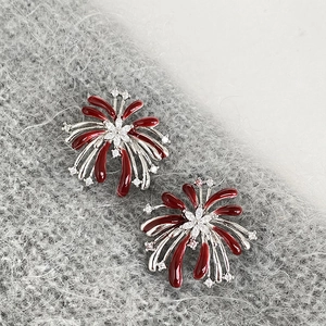 Nahaufnahme von roten Emaille-Feuerwerk-Ohrringen mit Zirkon auf grauem Strickhintergrund