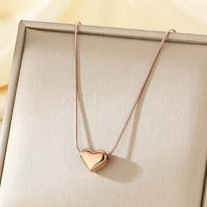 Collier cœur en or rose avec chaîne serpent présenté dans un écrin de bijoux de couleur beige