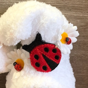 Close-up of white plush fabric featuring ladybug embroidery and daisy flower accents