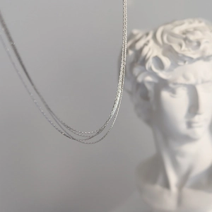 Artistic detail of layered silver titanium steel necklaces over a classic bust sculpture