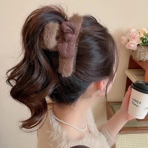 Detail of dark brown plush hair claw with a knit bow accessory worn on a model's head