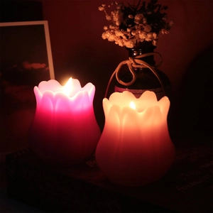 Dettaglio di candele profumate a forma di tulipano accese in rosso rosa e arancione chiaro
