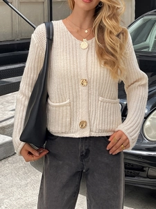 Détail d'un cardigan en maille blanc crème avec boutons dorés et deux poches avant