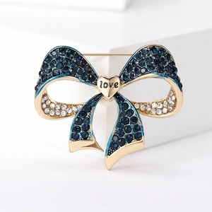 Close-up of golden bow brooch with blue and white crystals and a heart love charm