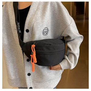 Detail of black canvas chest bag with vibrant orange zipper pulls on adjustable strap