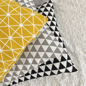 Detail of geometric cotton linen pillow covers in yellow, grey, and black on plush rug