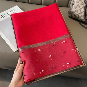 Detail of red silk-like scarf with pearl bead edges elegantly folded on a gold tray
