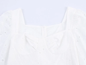 Détail de l'encolure carrée avec broderie ajourée délicate et texture plissée sur robe blanche