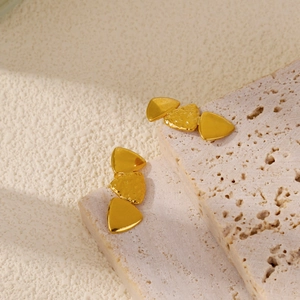 Close-up of golden geometric earrings with lava texture on travertine stone base