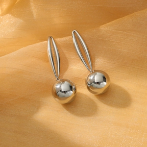 Polished silver hollow ball drop earrings made of titanium steel on gold fabric background