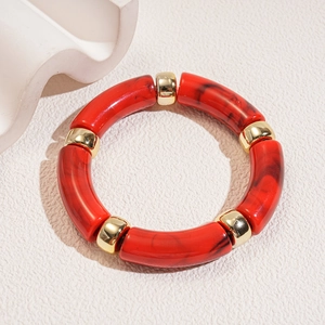 Macro shot of red marble acrylic segments and gold metal beads on a modern bracelet