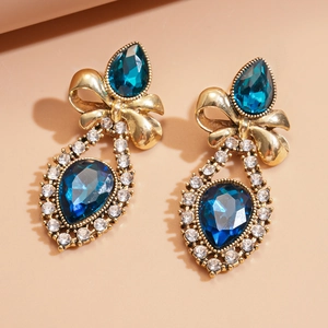 Detail of vintage gold bow earrings with a large blue teardrop gemstone and crystals