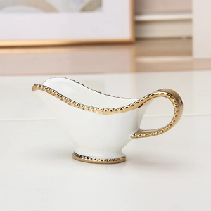 Close-up of a white ceramic creamer pitcher with elegant gold bead detailing on the rim