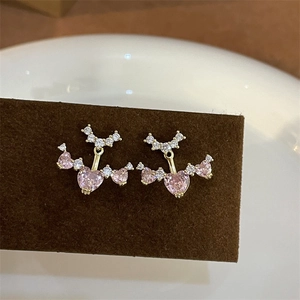 Detailed macro view of pink heart gemstone and wing design on golden earrings