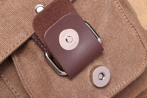 Close-up of canvas messenger bag with brown leather strap and silver magnetic buckle
