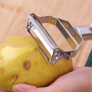 Stainless steel 2-in-1 peeler peeling a potato on a wooden background close-up