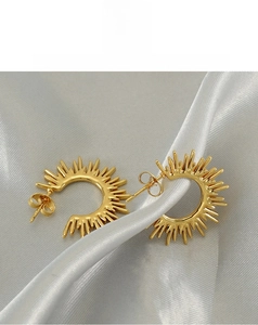 Detailed view of golden fan-shaped sunburst earrings on silver silk background
