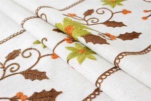 Detailed embroidery of brown branches and green leaves on natural beige linen tablecloth