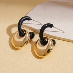 Detail of geometric C-shaped matte black earrings with polished gold oval charms on stone