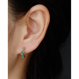 Close-up of a silver U-shaped earring with green zircon stones worn by a model