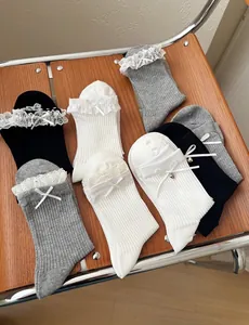 Detail of knit socks featuring delicate lace trim, ribbons and heart charms on wood