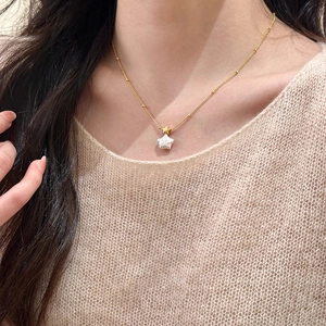 Collier étoile et perle plaqué or porté par un mannequin en pull beige