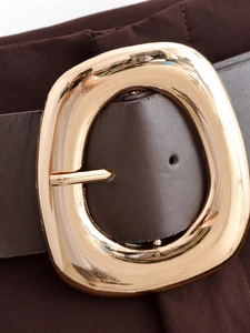 Dettaglio di una cintura vintage in pelle marrone con grande fibbia circolare dorata