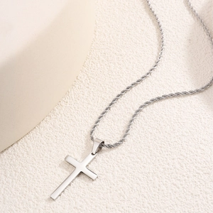 Dettaglio della catena a fune lucida con ciondolo a croce minimalista su base beige