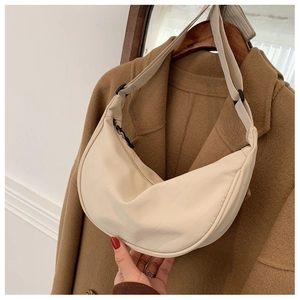 Detail of beige nylon crescent bag with adjustable wide strap shown against a wool coat
