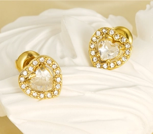 Close-up of golden double-layered heart-shaped earrings with rhinestones on white fabric
