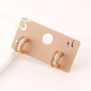 Detail of C-shaped gold hoop earrings with square clear stones on a display card