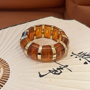 Macro shot of amber acrylic bracelet with gold metal links on a vintage folding fan background