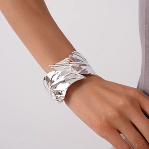 Close-up of a wide silver textured leaf cuff bracelet on a model's wrist