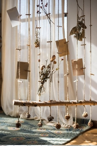 Detail of natural birch wood wall decor with hemp ropes, dried flowers, and pine cones