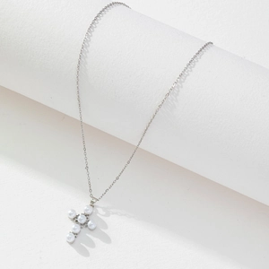 Detailed view of silver cross pendant necklace with pearls on a geometric display