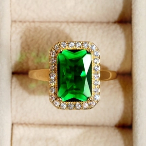 Close-up of gold ring featuring emerald green rectangle stone and halo crystal settings