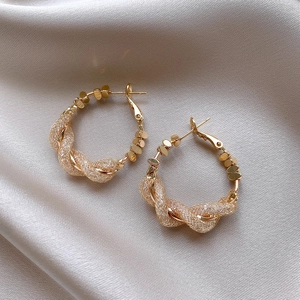 Close-up of golden intertwined hoop earrings with mesh texture on satin fabric