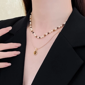 Detail of layered gold-plated necklace with brown tiger eye pendant on a black blazer