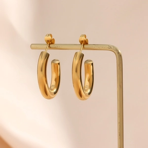 Detailed close-up of golden hollow hoop earrings on a metal jewelry display stand