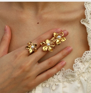 Detail of three golden flower rings with pearls worn by a model on white lace