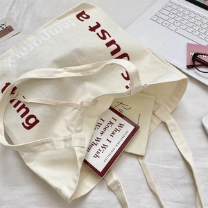 Gros plan d'un sac cabas en toile crème avec texte rouge sur un lit blanc décoré