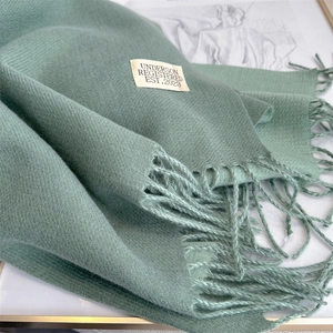 Close-up of light green cashmere scarf texture with tassel detail and brand label