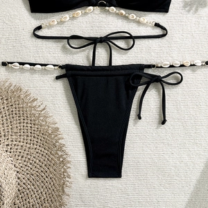 Detail of black ribbed bikini with white shell ornaments and side-tie bows on white fabric