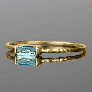 Detail of emerald-cut cyan gemstone on a handcrafted hammered gold geometric ring band