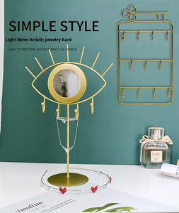Detailed view of eye-shaped gold metal jewelry stand with mirror and wall-mounted hooks