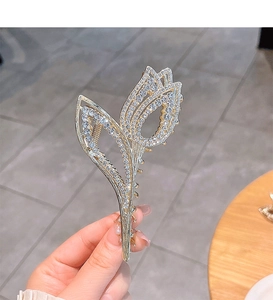 Detail of tulip hair claw clip in gold alloy with sparkling rhinestones held by hand