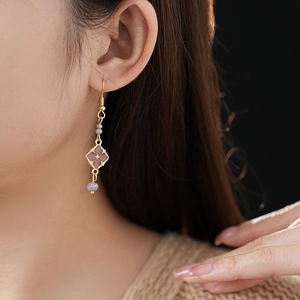 Detail of vintage gold earrings with purple clover charms and bead accents on a model